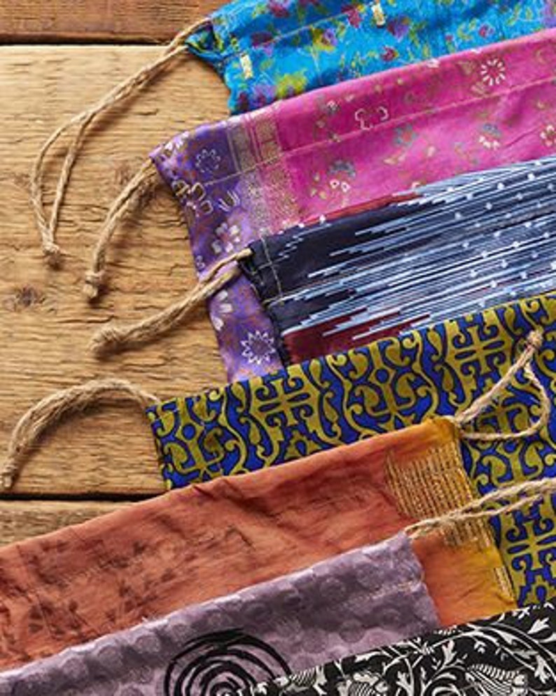 May include: A set of colorful fabric pouches with drawstring closures. The pouches are made from different patterned fabrics, including floral, geometric, and paisley designs. The pouches are tied together with twine.