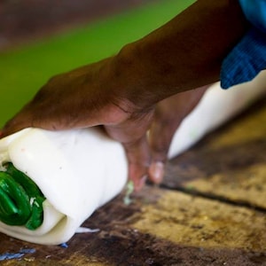 May include: A person rolling a white and green candle with their hand. The candle is being rolled on a wooden surface.