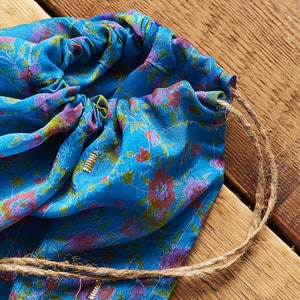 May include: A blue drawstring bag with a floral pattern and a brown cord. The bag is made of a soft, silky fabric.