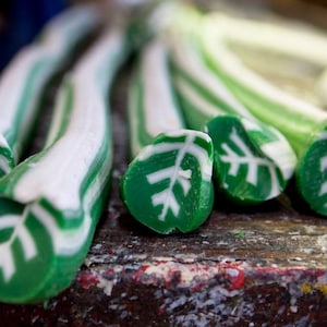 May include: Close-up of five green and white striped candy canes with a leaf design on the ends. The candy canes are arranged in a row on a wooden surface.
