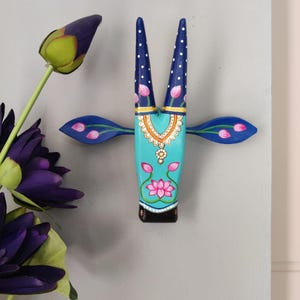 Pode incluir: Decora&ccedil;&atilde;o de parede de madeira pintada &agrave; m&atilde;o em forma de cabe&ccedil;a de touro. A cabe&ccedil;a &eacute; turquesa com desenhos florais e geom&eacute;tricos em rosa, branco e dourado. Os chifres s&atilde;o azul escuro com bolinhas brancas. As orelhas s&atilde;o azuis com detalhes florais rosa.