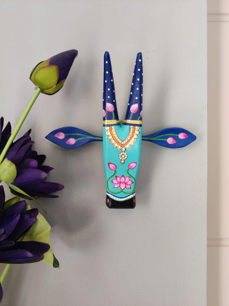 Pode incluir: Decora&ccedil;&atilde;o de parede de madeira pintada &agrave; m&atilde;o em forma de cabe&ccedil;a de touro. A cabe&ccedil;a &eacute; turquesa com desenhos florais e geom&eacute;tricos em rosa, branco e dourado. Os chifres s&atilde;o azul escuro com bolinhas brancas. As orelhas s&atilde;o azuis com detalhes florais rosa.