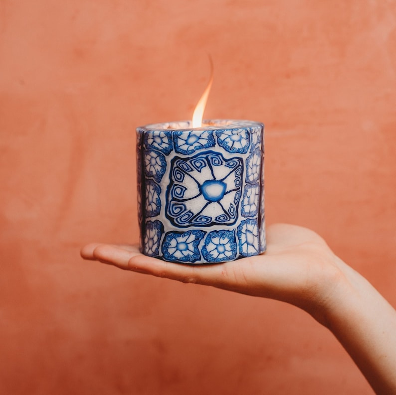 May include: A white candle with a blue and white patterned design. The candle is lit and the flame is visible.
