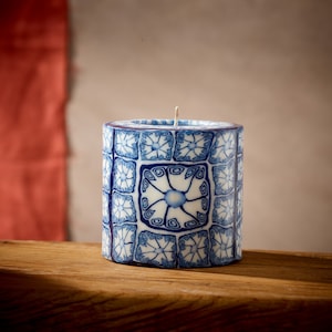 May include: A blue and white patterned candle with a geometric design. The candle is cylindrical and has a white wax base.