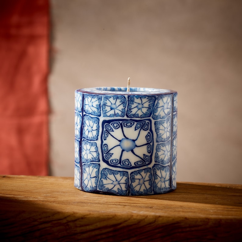 May include: A blue and white patterned candle with a geometric design. The candle is cylindrical and has a white wax base.