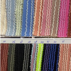 May include: A fabric swatch card featuring various colors of textured fabric with a wavy trim. Colors include beige, blue, green, orange, pink, brown, black, purple, and neon green. Numbers 17-33 are visible.