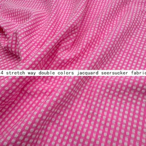 May include: A bright pink and white seersucker fabric featuring a small, repeating checkered pattern. The material has a textured, puckered surface and is labelled as 4 stretch way double colours jacquard seersucker fabric in the image.