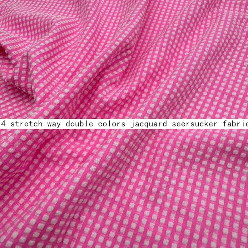 May include: A bright pink and white seersucker fabric featuring a small, repeating checkered pattern. The material has a textured, puckered surface and is labelled as 4 stretch way double colours jacquard seersucker fabric in the image.