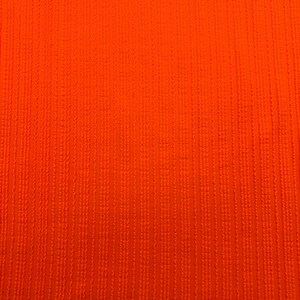 May include: Close-up of a vibrant orange fabric with a textured, vertical ribbed pattern. The color is a bright, solid hue, and the texture suggests a woven or knitted material. The image is well-lit, highlighting the details of the fabric.