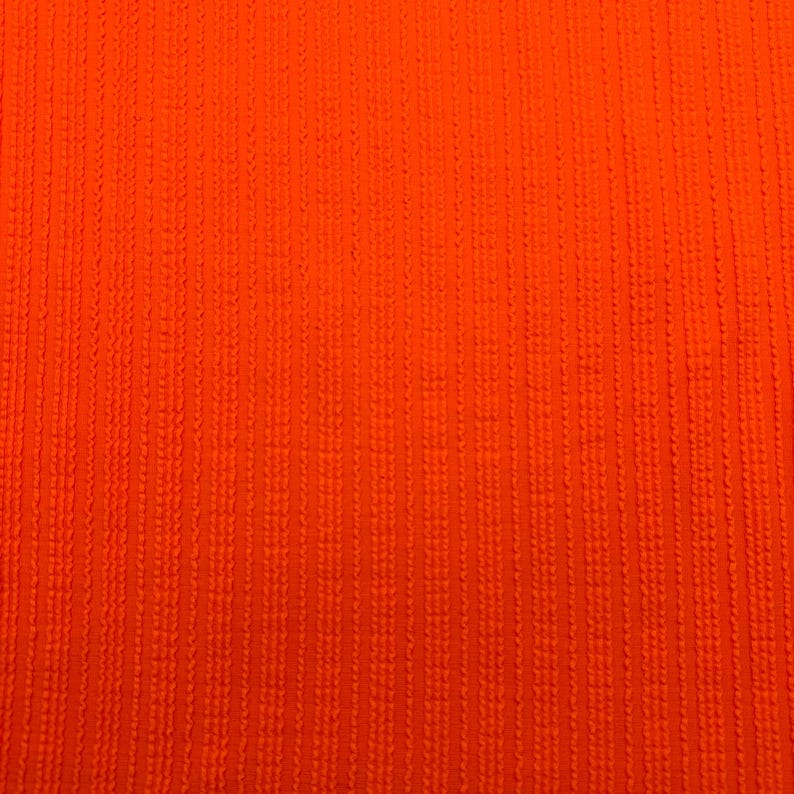 May include: Close-up of a vibrant orange fabric with a textured, vertical ribbed pattern. The color is a bright, solid hue, and the texture suggests a woven or knitted material. The image is well-lit, highlighting the details of the fabric.