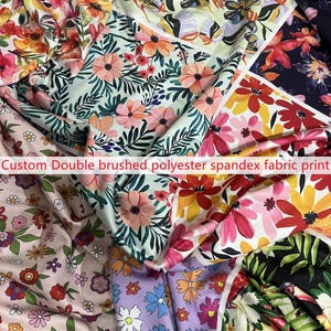 May include: A collection of double brushed polyester spandex fabric prints featuring various floral patterns. The designs include colorful blossoms in shades of pink, red, yellow, and blue against backgrounds of black, white, light green, and lavender.