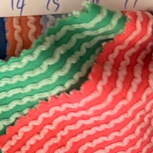 May include: Close-up of fabric samples with a wavy, textured design. The samples feature a repeating pattern of white lines on a green and coral background. The edges are scalloped. Numbers 14, 15, 16, and 17 are visible.