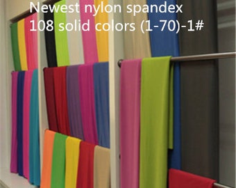 Puede incluir: Una muestra de 108 telas de color sólido, etiquetadas como "Newest nylon spandex 108 solid colors (1-70)-1#", colgadas en una pared blanca.