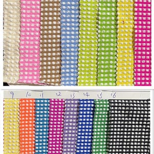 May include: A collection of sixteen fabric swatches arranged in two rows, each featuring a textured, raised dot pattern in a grid. The colours include beige, pink, tan, light blue, lime green, yellow, magenta, orange, cyan, purple, and black.
