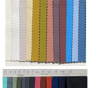 Op de afbeelding: Een kleurstaalkaart met 25 stofstalen in verschillende kleuren. De stof wordt beschreven als 4-weg stretch, 80% polyester, 20% elastaan, enkelzijdig geborsteld, zacht aanvoelend, 155 cm breed en 200 g/m². De kaart is genummerd van 1 tot en met 25.