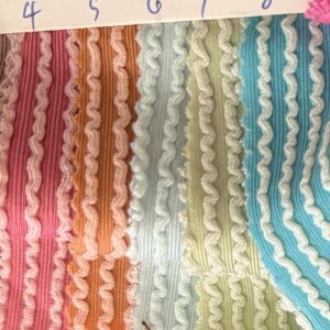 May include: Close-up of fabric swatches in various colors, including pink, orange, light blue, and yellow. Each swatch has a ribbed texture with a wavy, white trim along the edges. Numbers 4 through 9 are visible at the top.