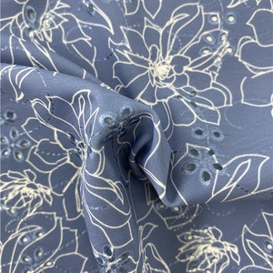 Op de afbeelding: Blauwe stof met een wit bloemenpatroon en oogletdetails. De stof is zacht en heeft een subtiele glans.