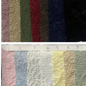 Può includere: Un campionario di tessuti con campioni di tessuto strutturato in vari colori. I colori includono rosa, azzurro, bianco, giallo, beige, verde, malva, marrone chiaro, verde oliva, bordeaux, marrone, blu navy e nero. Il tessuto ha un motivo increspato e in rilievo.