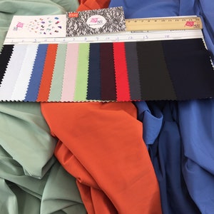 May include: A fabric swatch card featuring fourteen distinct colors of ribbed material, numbered one through fourteen, displayed alongside a wooden ruler measuring 15 centimeters. The swatches include black, white, blue, orange, green, pink, and red.