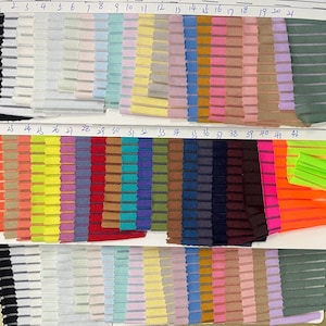 Puede incluir: Una carta de colores de tela con cuarenta y dos muestras numeradas de material plisado y a rayas. La colección muestra un amplio espectro de colores, incluyendo pasteles, neones vibrantes, tonos primarios y tonos tierra, dispuestos en filas.