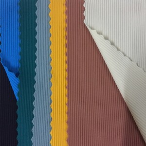May include: A collection of ribbed fabric swatches in vertical strips of black, blue, dark teal, grey, yellow, terracotta, and cream. The top edge features a white paper header with the handwritten numbers 15, 16, 17, 18, 19, and 20.
