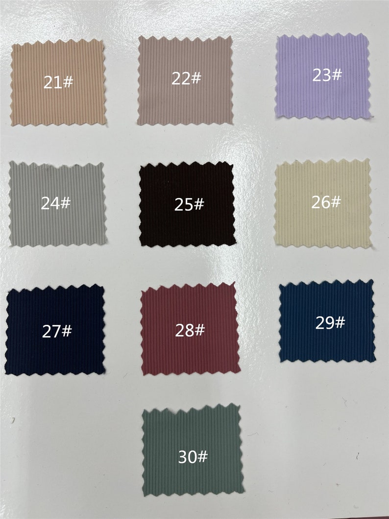 May include: A collection of ten rectangular fabric swatches with pinked edges, each featuring a vertical ribbed texture. The swatches are labeled with numbers 21# through 30# and display a variety of colors including beige, gray, lavender, black, cream, navy, maroon, and sage green.