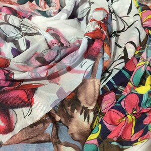 May include: A white, pink and blue floral patterned scarf with a red floral pattern on one side. The scarf is made of a soft, sheer fabric.