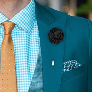 Könnte beinhalten: Ein blauer Anzugsakko in Teal mit einer grauen Weste und einem weiß-blau karierten Hemd. Der Mann trägt eine braune gemusterte Krawatte und eine schwarze Blumen-Reversnadel.