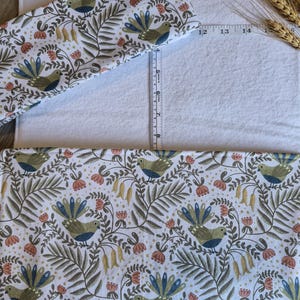 May include: White changing mat cover with a colorful bird and floral pattern. The pattern includes birds with blue and green feathers, red flowers, and green leaves. A ruler shows the mat is approximately 35 cm long.