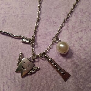 May include: A silver necklace with a charm of a smiling tooth with wings, a toothbrush, a tube of toothpaste that says "toothpaste", and a pearl.