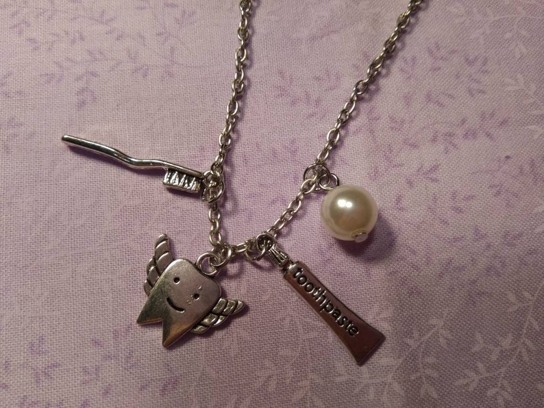 May include: A silver necklace with a charm of a smiling tooth with wings, a toothbrush, a tube of toothpaste that says "toothpaste", and a pearl.
