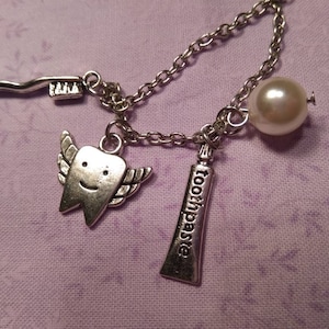 May include: A silver charm necklace with a pearl, a toothbrush, a tube of toothpaste that says "toothpaste", and a smiling tooth with wings.