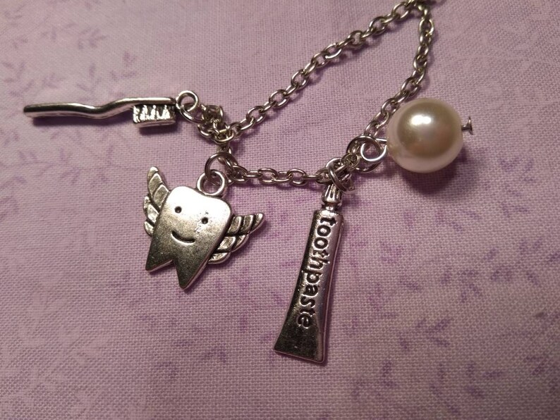 May include: A silver charm necklace with a pearl, a toothbrush, a tube of toothpaste that says "toothpaste", and a smiling tooth with wings.