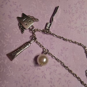 May include: A silver necklace with a charm of a tooth with a smiley face, a charm of a tube of toothpaste that says "toothpaste", a charm of a toothbrush, and a pearl.
