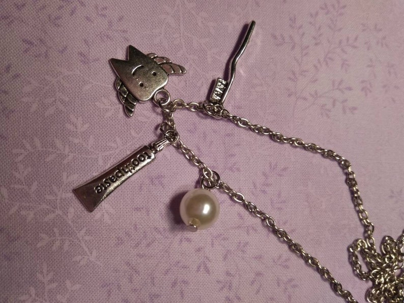 May include: A silver necklace with a charm of a tooth with a smiley face, a charm of a tube of toothpaste that says "toothpaste", a charm of a toothbrush, and a pearl.