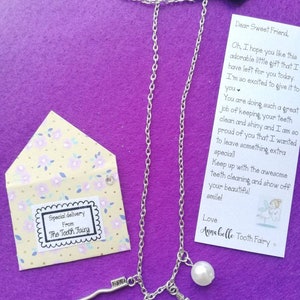 May include: A silver necklace with a tooth charm, a pearl, a toothbrush charm, and a small silver stick charm. The necklace comes with a note from the Tooth Fairy that says "Dear Sweet Friend, Oh, I hope you like this adorable little gift that I have left for you today. I'm so excited to give it to you. You are doing such a great job of keeping your teeth clean and shiny and I am so proud of you that I wanted to leave something extra special! Keep up with the awesome teeth cleaning and show off your beautiful smile! Love Annabelle Tooth Fairy"