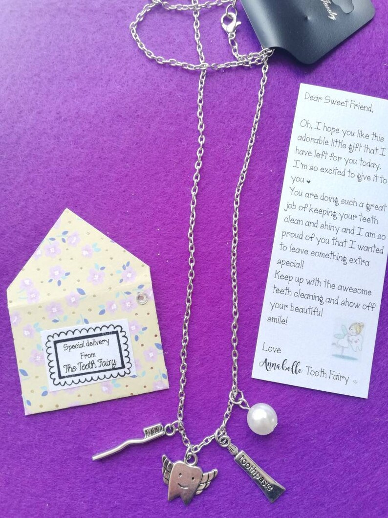 May include: A silver necklace with a tooth charm, a pearl, a toothbrush charm, and a small silver stick charm. The necklace comes with a note from the Tooth Fairy that says "Dear Sweet Friend, Oh, I hope you like this adorable little gift that I have left for you today. I'm so excited to give it to you. You are doing such a great job of keeping your teeth clean and shiny and I am so proud of you that I wanted to leave something extra special! Keep up with the awesome teeth cleaning and show off your beautiful smile! Love Annabelle Tooth Fairy"