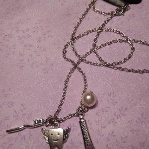 May include: A silver chain necklace with a tooth charm, a toothbrush charm, a pearl charm, and the word "toothpaste" on the toothbrush charm.
