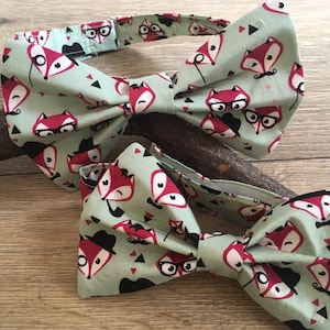 May include: Two bow ties with a green background and a pattern of red foxes wearing glasses, hats, and mustaches.