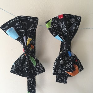 May include: Two black bow ties with a white background and mathematical equations and symbols printed on them. The bow ties have a blue, green, red, and orange accent.