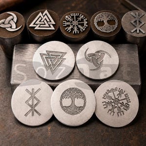 Może przedstawiać: Kolekcja metalowych stempli z różnymi symbolami nordyckimi, w tym Valknut, Vegvisir i wzór Drzewa Życia. Stemple są okrągłe i cylindryczne, z szczegółowymi grawerunkami. Tło to ciemna, teksturowana powierzchnia.