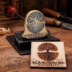 May include: A wooden stamp with a tree design and the text "SCANDINAVIAN HANDCRAFT" is shown next to a wooden block with the same design. The stamp is on a metal base with a wooden handle. The background includes woodworking tools.