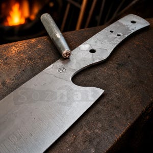 Puede incluir: Un cuchillo de metal parcialmente construido con un mango texturizado y una herramienta de metal a juego. La hoja del cuchillo es plateada con un mango curvo y varios agujeros. El fondo muestra una forja borrosa.