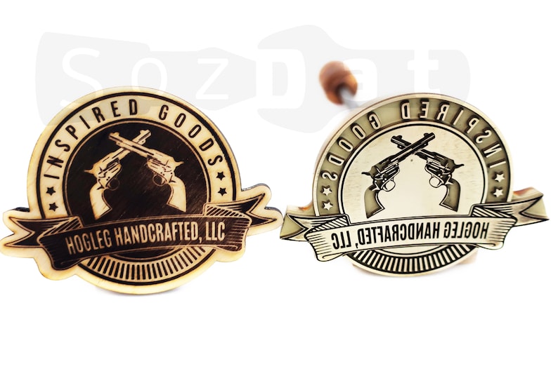 May include: Two wooden branding irons with a circular design featuring crossed revolvers and the text "INSPIRED GOODS" and "HOGLEG HANDCRAFTED, LLC". One iron is light wood, the other is metallic.