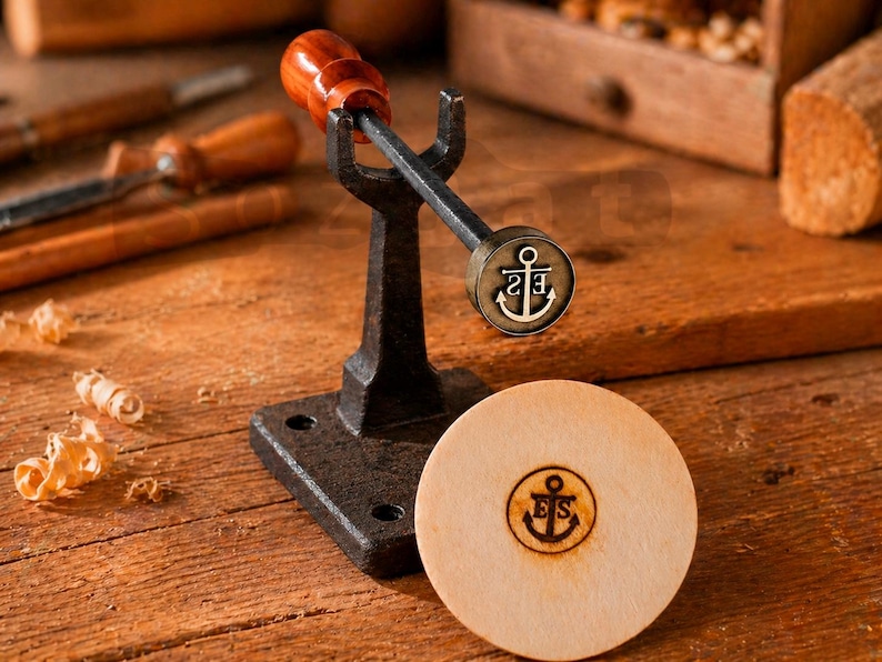 May include: A woodworking tool with a dark metal base and handle, topped with a wooden handle. The tool has an anchor emblem. A wooden disc with the same anchor emblem is next to the tool. The background includes other woodworking tools.