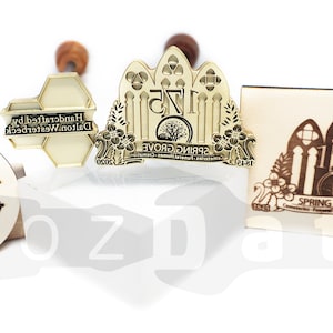 May include: A collection of custom stamps with wooden handles. The stamps feature intricate designs, including text that reads "Handcrafted by Dalton Westerbeck" and "Spring Grove 175". The stamps are in various shapes and sizes.