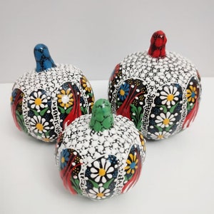 Peut inclure: Trois citrouilles décoratives en céramique avec des motifs floraux complexes dans des tons de rouge, bleu, vert, blanc et noir. Les citrouilles sont peintes à la main et ont une finition brillante.