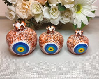 May include: Three orange ceramic pomegranate ornaments with blue evil eye designs. The pomegranates are speckled with white and black paint.