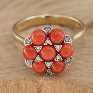 May include: A gold ring with a cluster of red coral stones and small diamonds set in a flower shape.