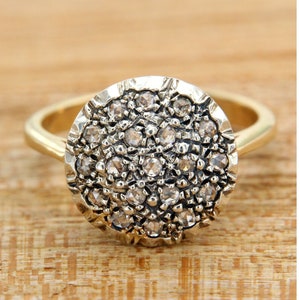 Può includere: Un anello d'oro con una montatura rotonda e testurizzata incrostata di piccoli diamanti trasparenti.